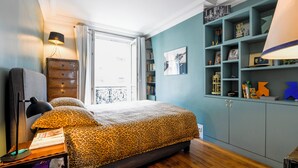 A bedroom with a bed, a dresser, a lamp, and a bookshelf.