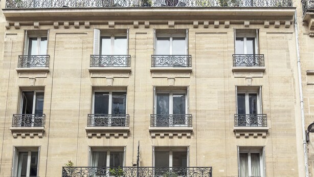A multi-story building with balconies, a storefront, and a sign for 'Arnaud Larher'.