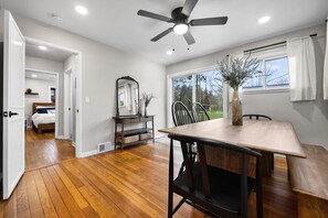 A room with a wooden floor, a dining table with chairs, a ceiling fan, and a large window with curtains. - NEW Bellaire Home, 5 Minute WALK to downtown! (Bellaire)