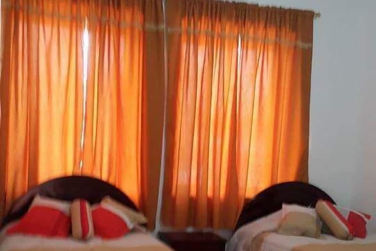 Una habitación con dos camas, cortinas naranjas y suelo de baldosas.