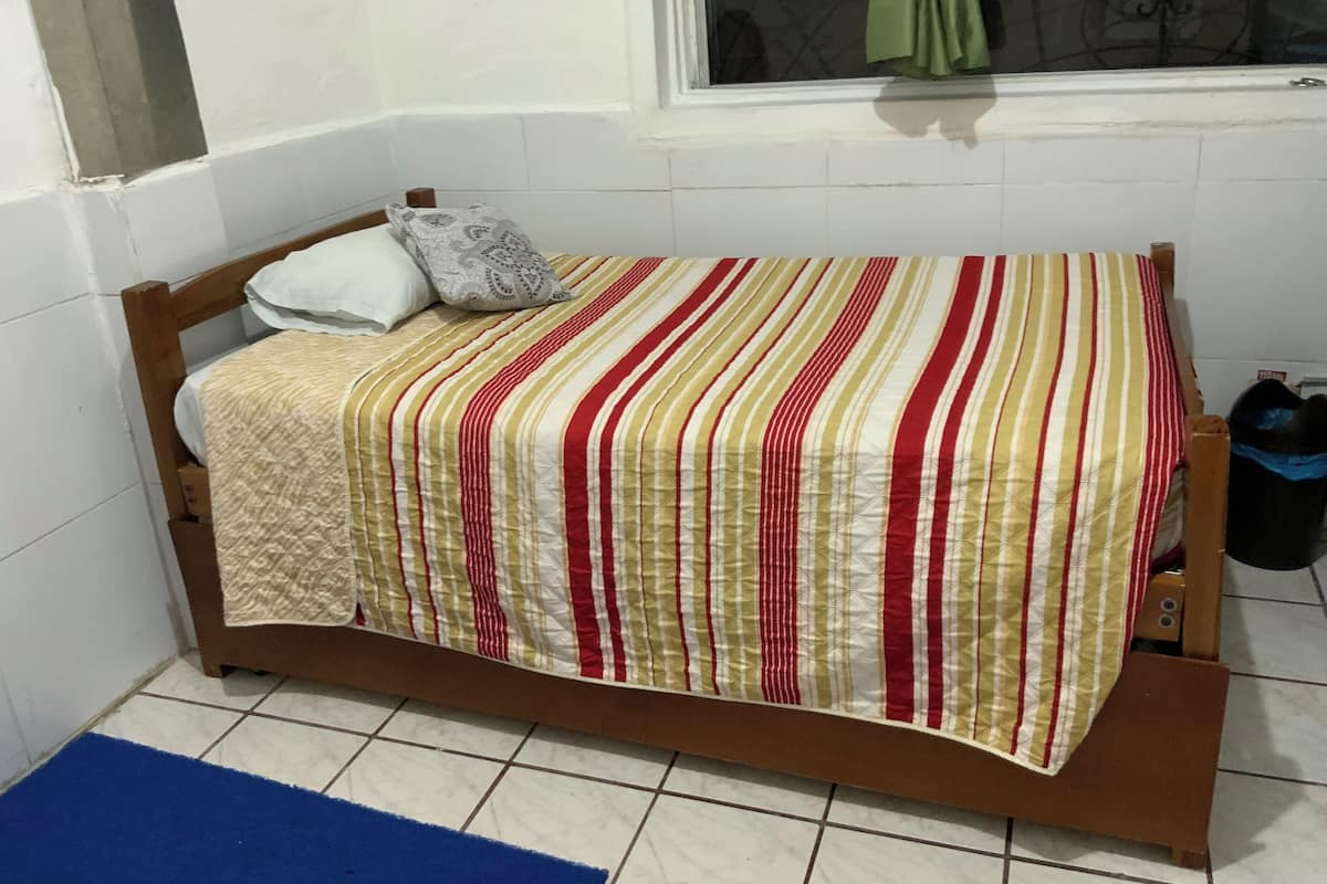 Una habitación pequeña con una cama individual, un cabecero de madera, una colcha a rayas y una alfombra azul en el suelo.