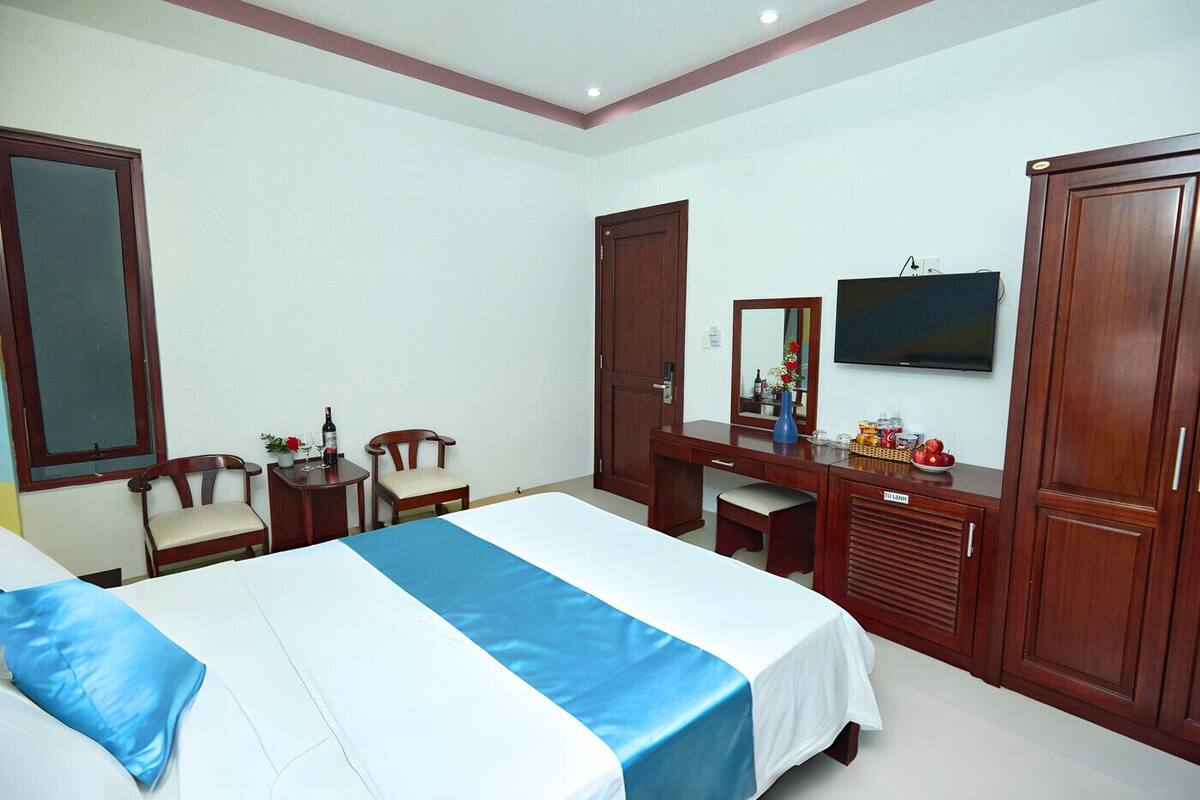 A hotel room with a bed, a desk, a chair, a wardrobe, a television, and a window.