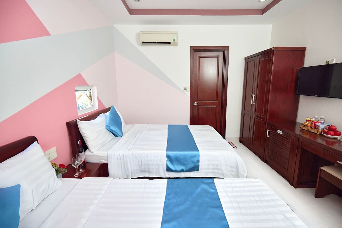A hotel room with two beds, a wooden wardrobe, a television, and a small table with fruit and snacks.