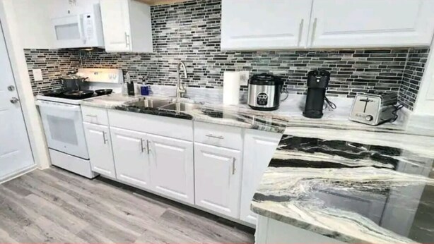A modern kitchen with white cabinets, a marble countertop, and a brick backsplash. - #13 Clearwater airport home (Clearwater)