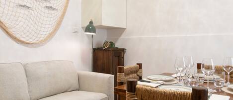 A dining area with a wooden table set for four, a woven chair, a sofa, and a wall-mounted fish net decoration.
