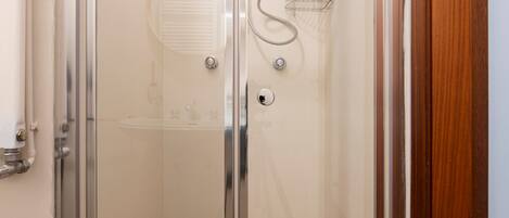 A glass-enclosed shower with a metal rack and a small shelf.