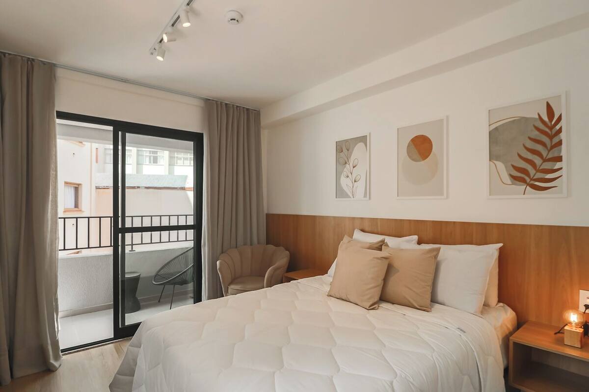 A hotel room with a large bed, a chair, a nightstand, and a view of the outside balcony.