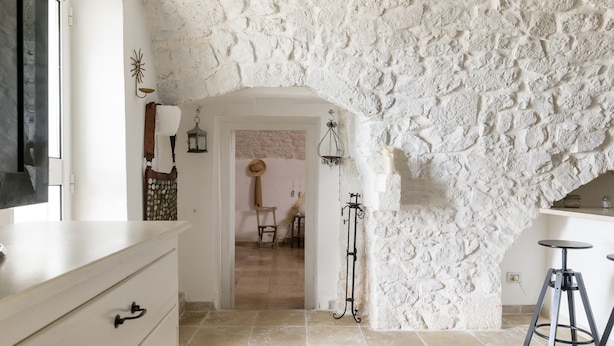 A room with a stone wall, a wooden door, a white dresser, and a bar area with stools. - Terrazza Olivia Maria by Wonderful Italy (Ostuni)
