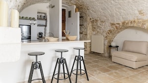 A rustic interior with a stone ceiling, a kitchenette, a sofa, and three stools. - Terrazza Olivia Maria by Wonderful Italy (Ostuni)