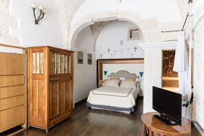 Een slaapkamer met een houten garderobe, een bed met een bedovertrek met patroon, een televisie op een klein tafeltje en een stenen muur met een open haard.