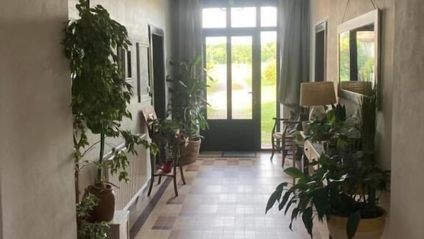 A hallway with tiled flooring, potted plants, and a large window at the end. - L'intemporelle (Ozourt)