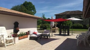 An outdoor patio with white chairs, a red umbrella, and a stone wall. - L'intemporelle (Ozourt)