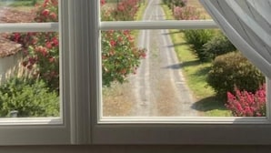 A room with a large window offering a view of a rural road and lush greenery. - L'intemporelle (Ozourt)