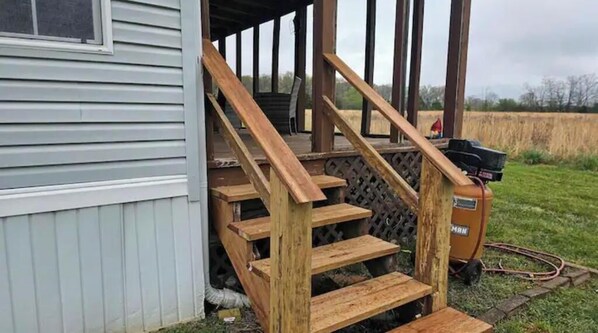A wooden staircase leading to a covered porch area with a generator outside.