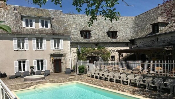 A pool area with a stone building, outdoor seating, and a fenced patio.