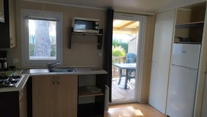 A compact kitchen with a microwave, sink, and a small refrigerator. There is a sliding door leading to an outdoor patio area.