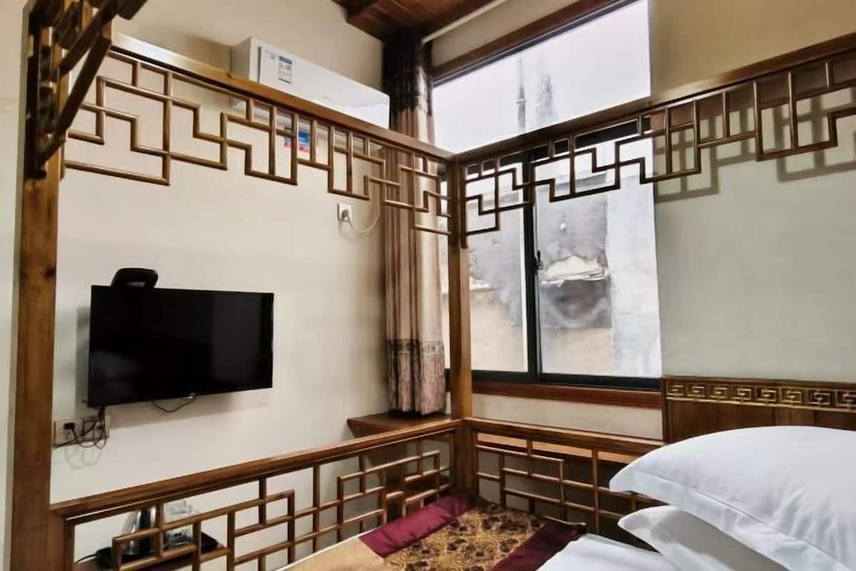 A room with a TV mounted on the wall, a window with a view, and a wooden decorative partition.