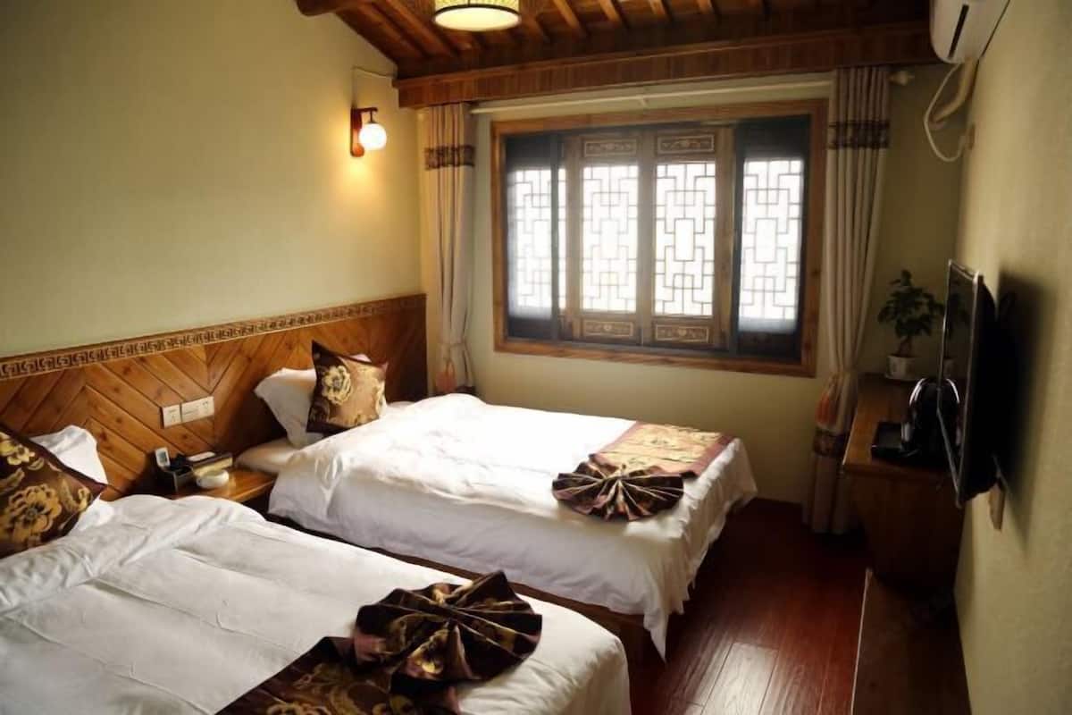 A hotel room with two beds, wooden headboard, a window with decorative lattice, and a television on the wall.