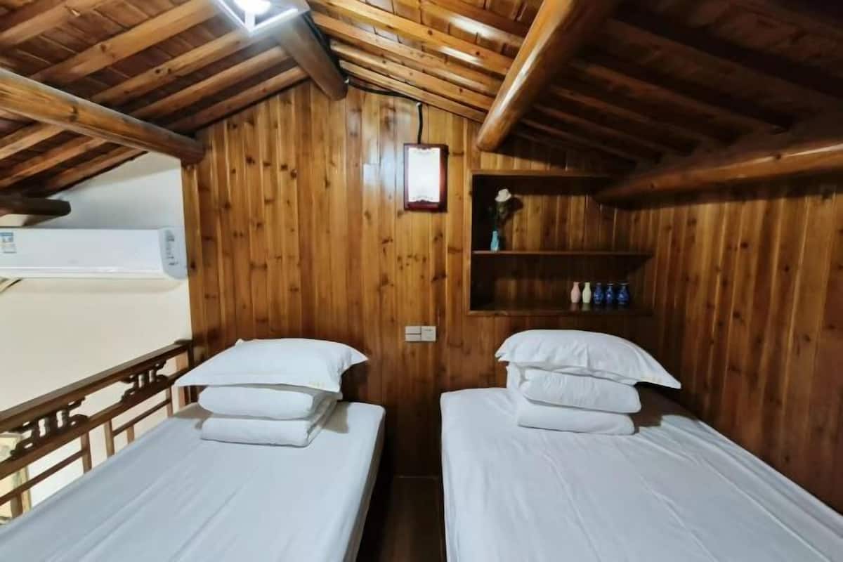 A wooden cabin with two single beds, a shelf with bottles, and a mounted picture.