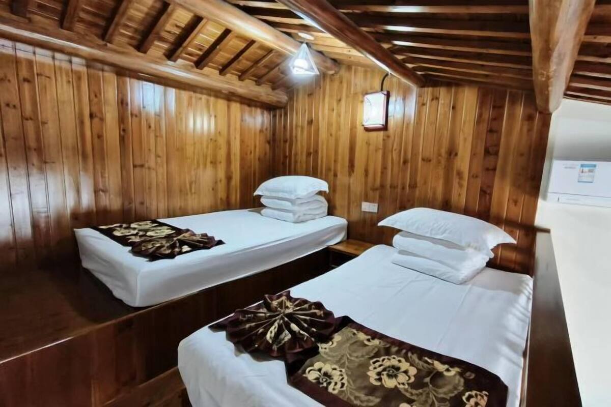 A wooden cabin room with two beds, a wooden ceiling, and a small window.