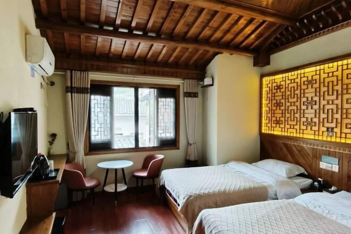 A hotel room with a wooden ceiling, two beds, a small table, a TV, and a decorative wall panel.
