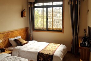 A hotel room with a bed, a nightstand, a window with curtains, and a wall-mounted lamp.