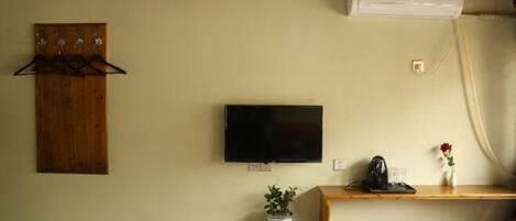 A room with a mounted TV, a wooden coat rack, a shelf with a potted plant, a small stool, and an air conditioning unit.