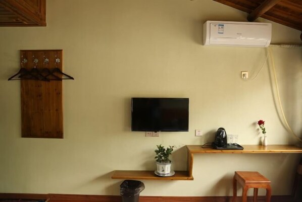 A room with a mounted TV, a wooden coat rack, a shelf with a potted plant, a small stool, and an air conditioning unit.