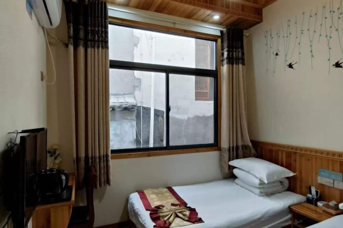 A room with a bed, a TV, a wooden headboard, a window with curtains, and a wall with hanging decorations.