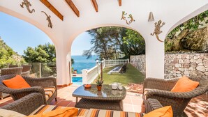 A covered patio with wicker furniture, a view of the sea, and a stone wall.