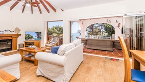 A spacious living room with a fireplace, a television, and a view of the sea through large windows.