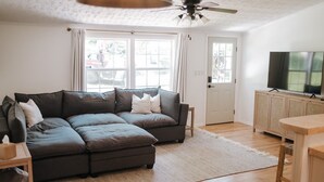 A living room with a sectional sofa, a television on a wooden cabinet, and a ceiling fan.