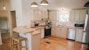 A modern kitchen with white cabinets, a central island, wooden stools, and stainless steel appliances.