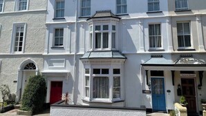 A row of white buildings with a central building featuring a bay window and a blue door labeled "Victoria House."