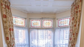 A corner room with two leather armchairs, a small table, and a bay window with stained glass.