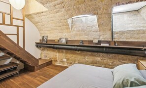 A bedroom with a wooden staircase, a bed with white bedding, and a stone wall. - A DESIGNER PLACE WITH PRIVATE PATIO IN THE HEART OF SAINT GERMAIN - RUE CLEMENT (Paris)