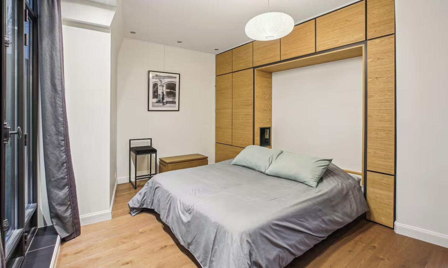 A modern bedroom with a bed, bedside table, and a wall-mounted panel.