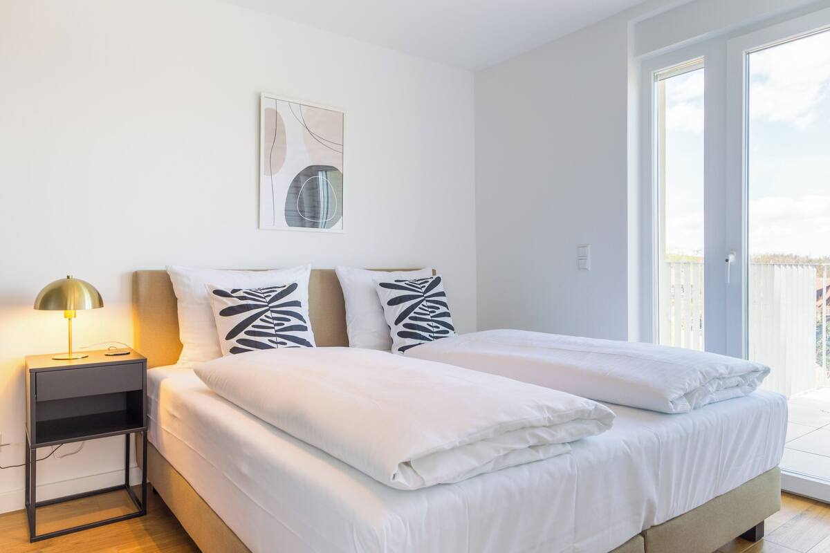 Un dormitorio moderno con una cama, una mesita de noche con lámpara y un ventanal grande.