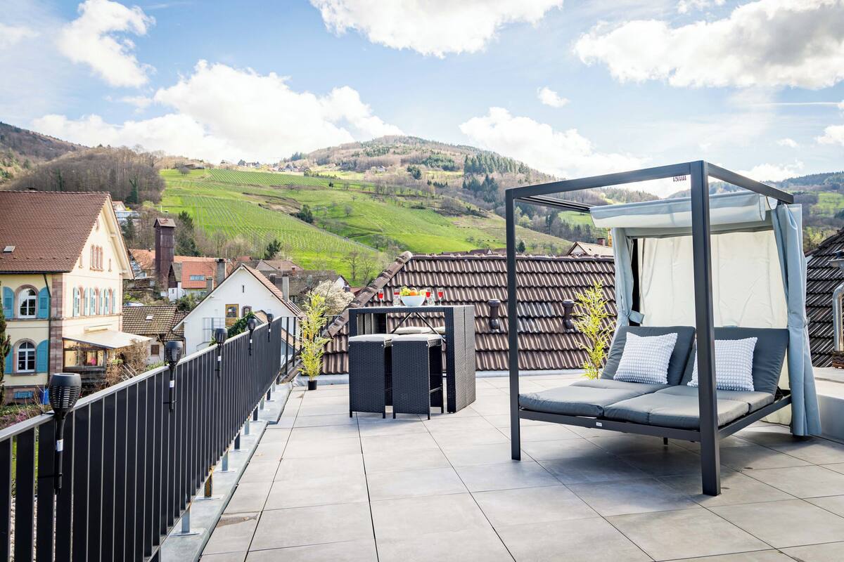 Terraza en la azotea con una silla colgante, una mesa y vistas a un viñedo y colinas.