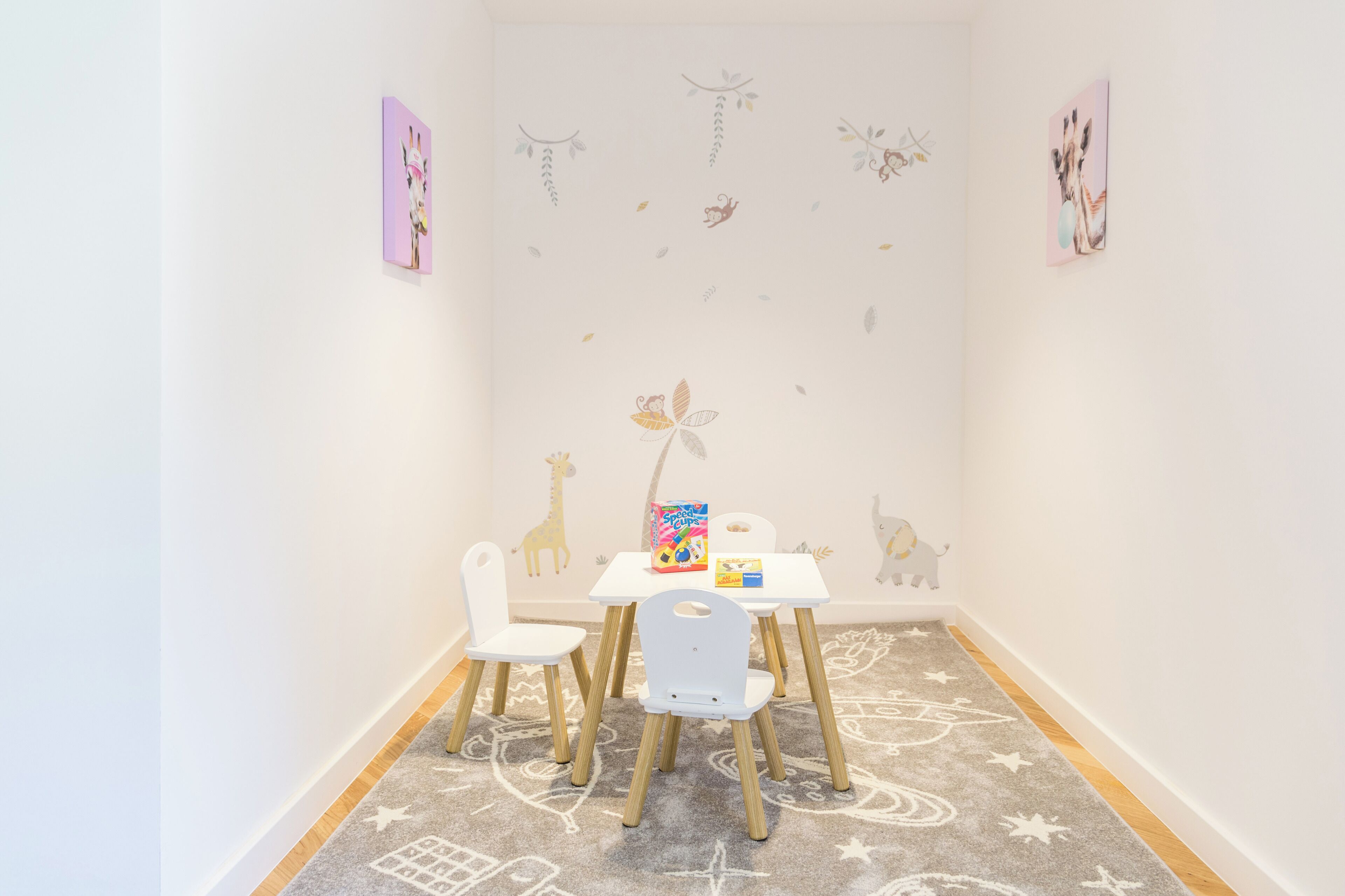 Una sala de juegos infantil con una mesa blanca, dos sillas y un colorido baúl de juguetes.