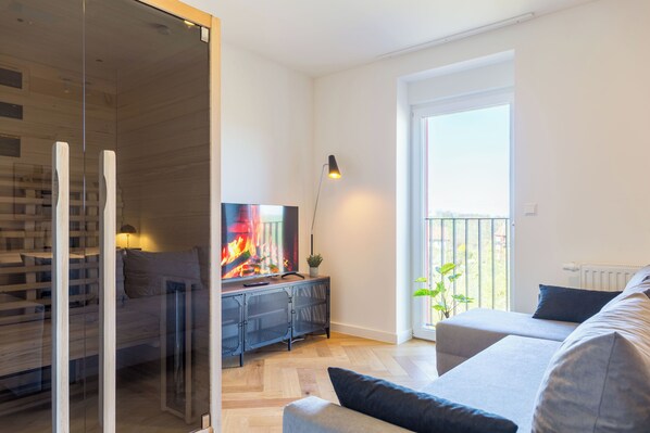 A modern living room with a flat-screen TV, a sofa, a coffee table, and a sliding glass door leading to a balcony. - Adler Apartments Sasbachwalden (Sasbachwalden)