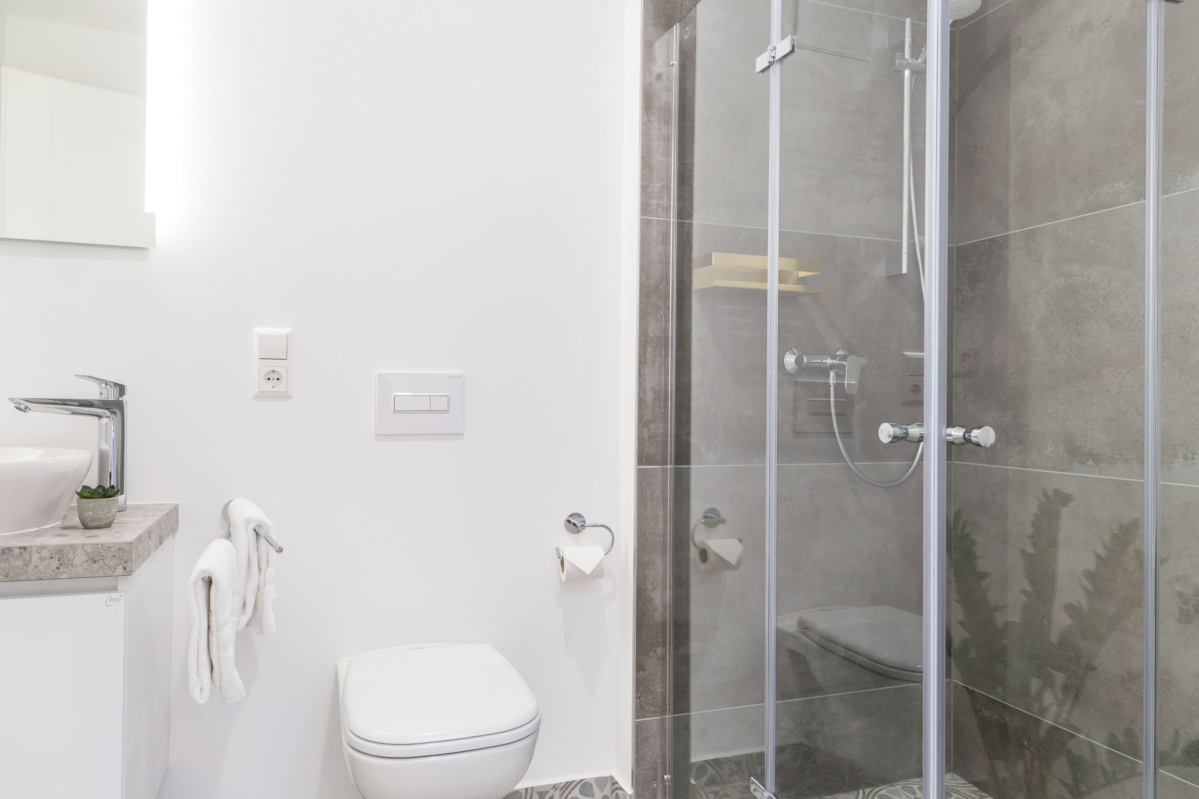 Ein modernes Badezimmer mit einer Duschkabine, einem weißen Waschbecken und einer Toilette.