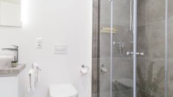 Ein modernes Badezimmer mit einer Duschkabine, einem weißen Waschbecken und einer Toilette.