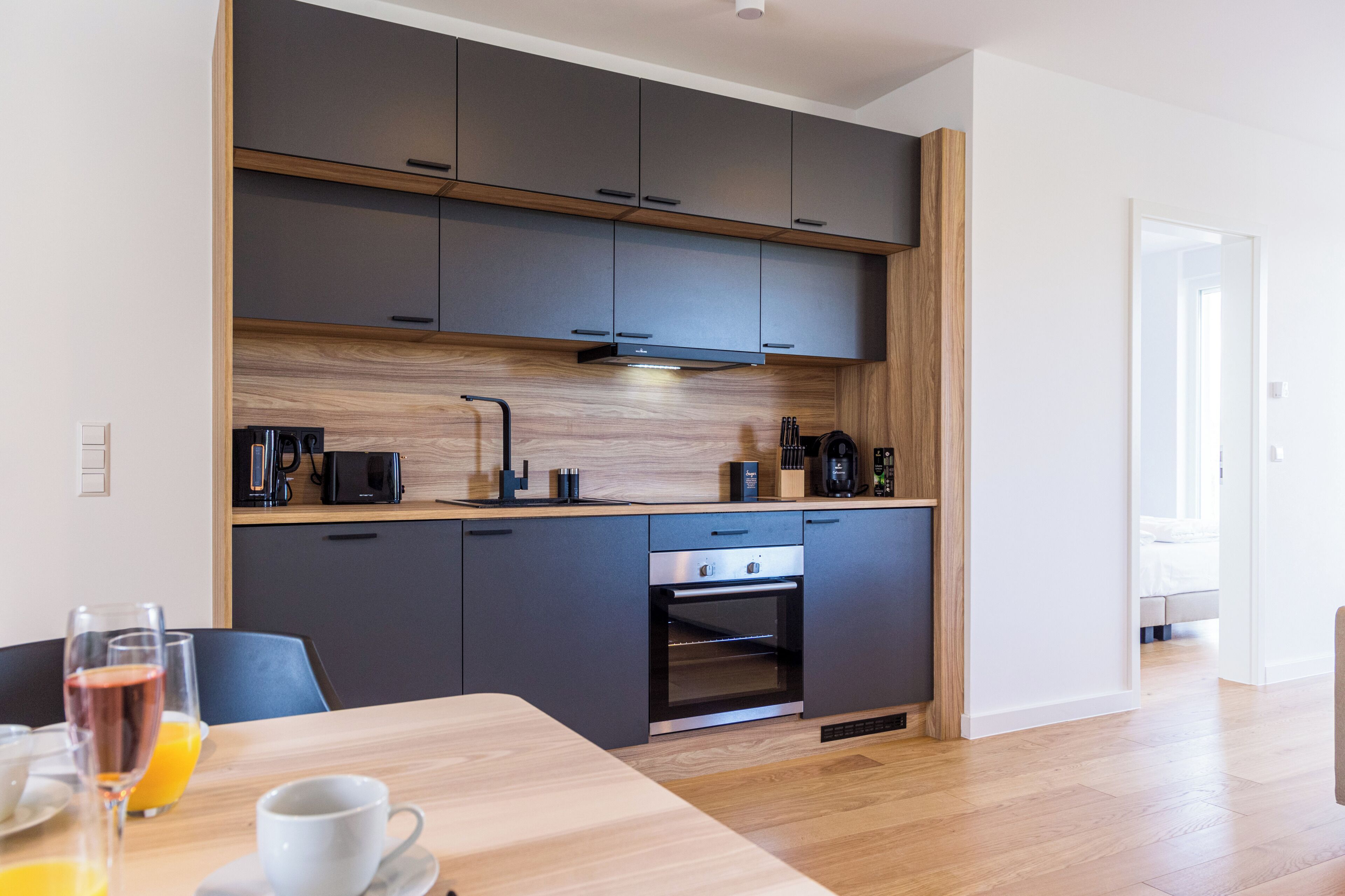Una cocina moderna con armarios oscuros, horno empotrado y encimera de madera.