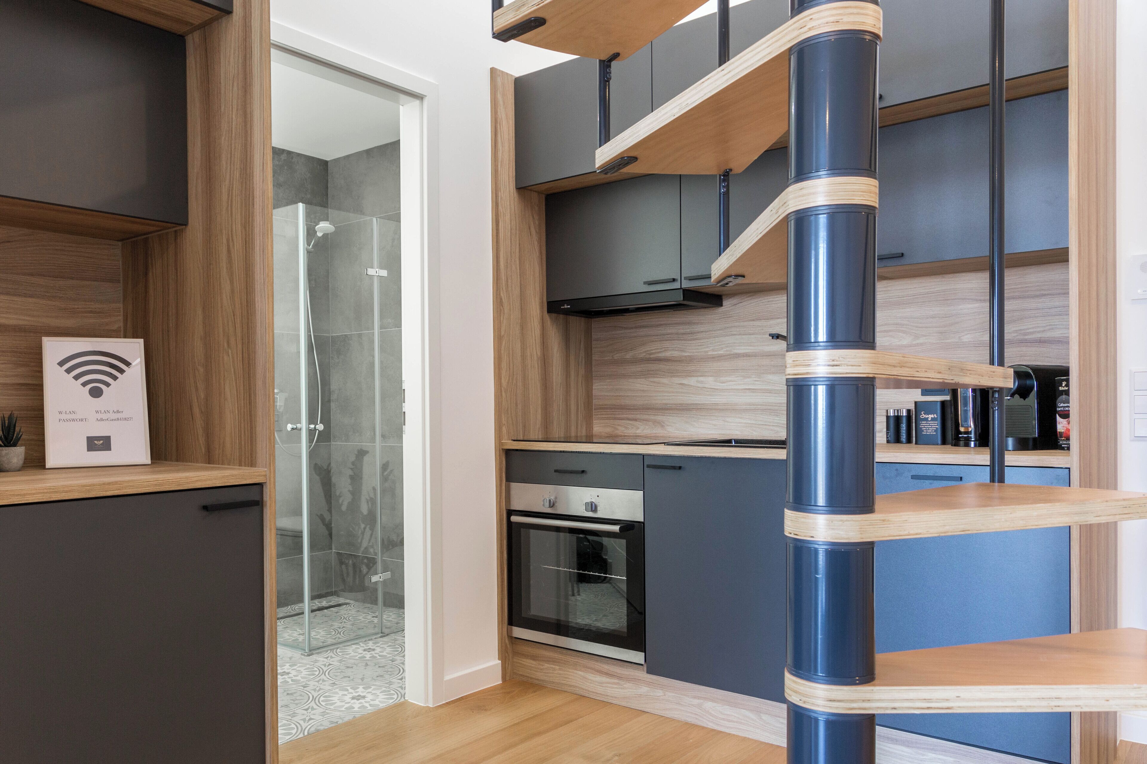 A modern kitchen with a built-in oven, a glass shower enclosure, and wooden cabinetry.