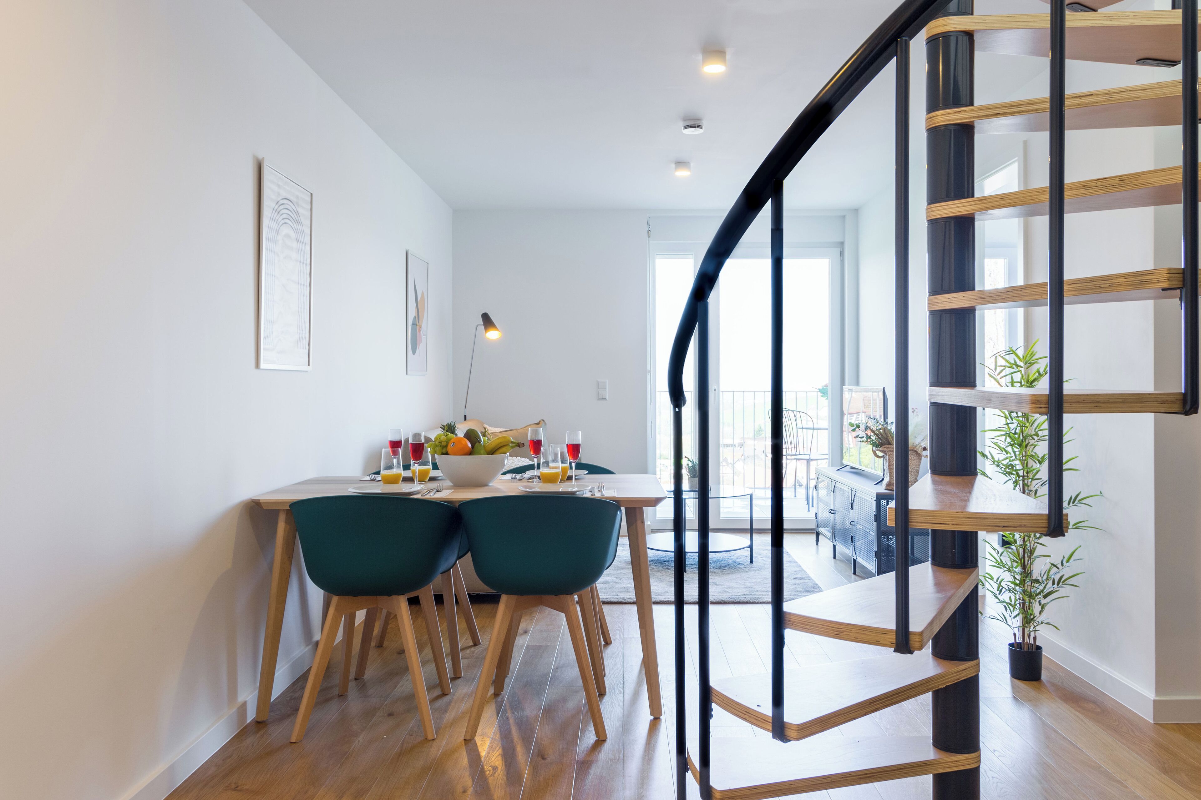 Eine moderne Küche mit Essbereich, inklusive einer Holztreppe, einem Esstisch mit Stühlen und Blick zum Wohnzimmer.