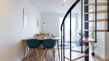 Eine moderne Küche mit Essbereich, inklusive einer Holztreppe, einem Esstisch mit Stühlen und Blick zum Wohnzimmer.