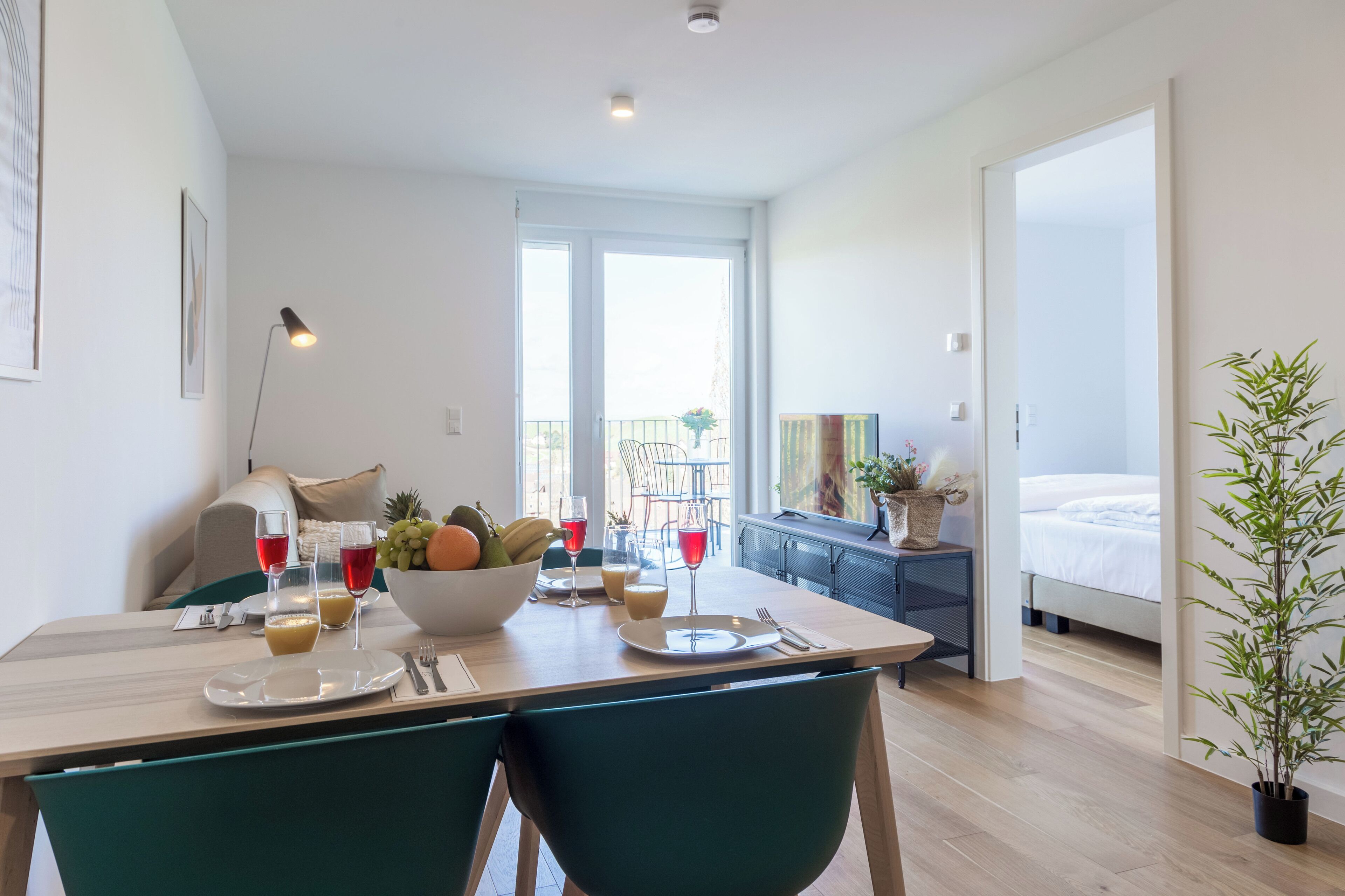 Un área de comedor con una mesa dispuesta para dos personas, un frutero y dos copas de vino tinto.