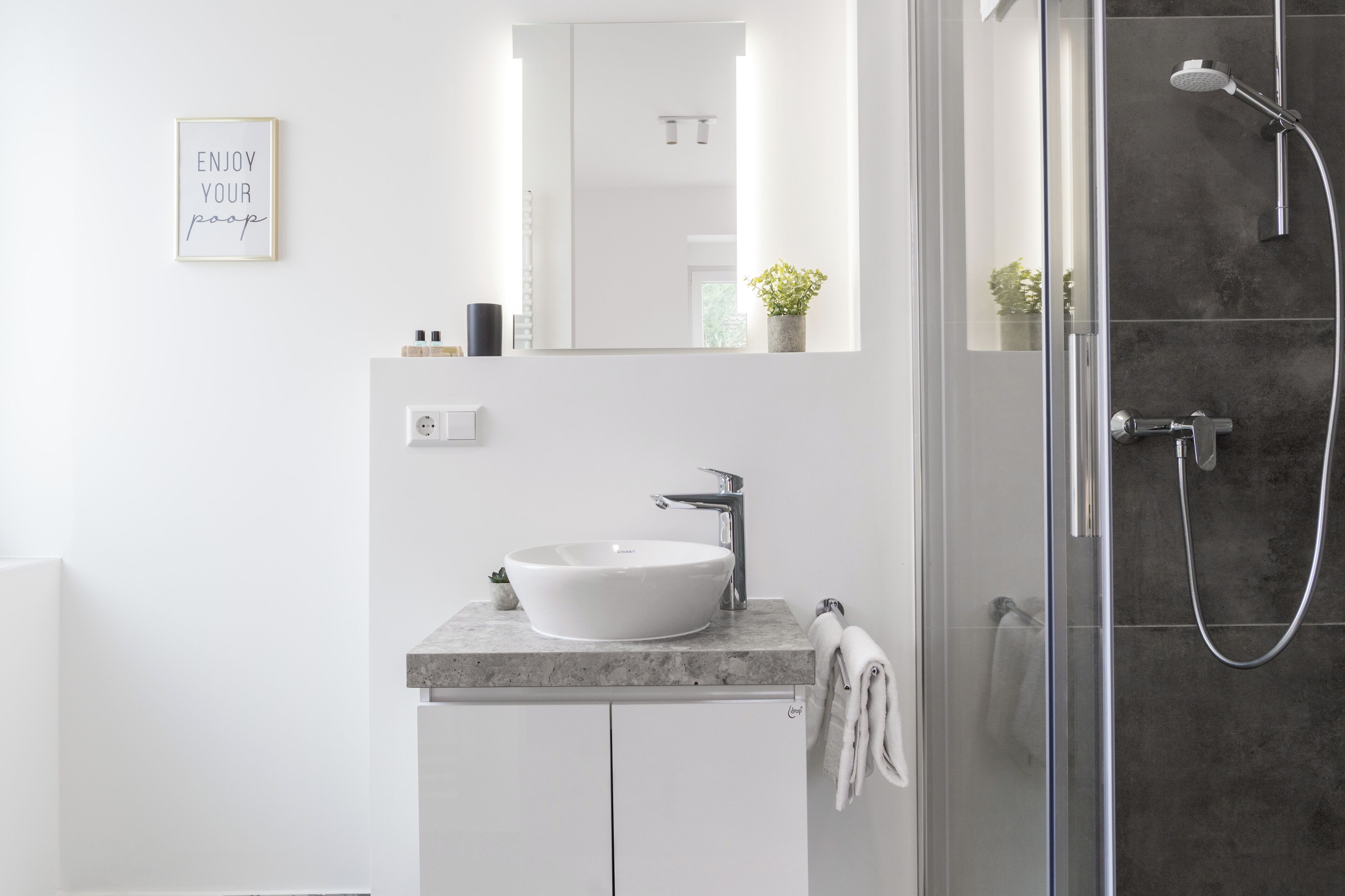 Un baño moderno con un lavamanos blanco, un espejo grande y una zona de ducha.
