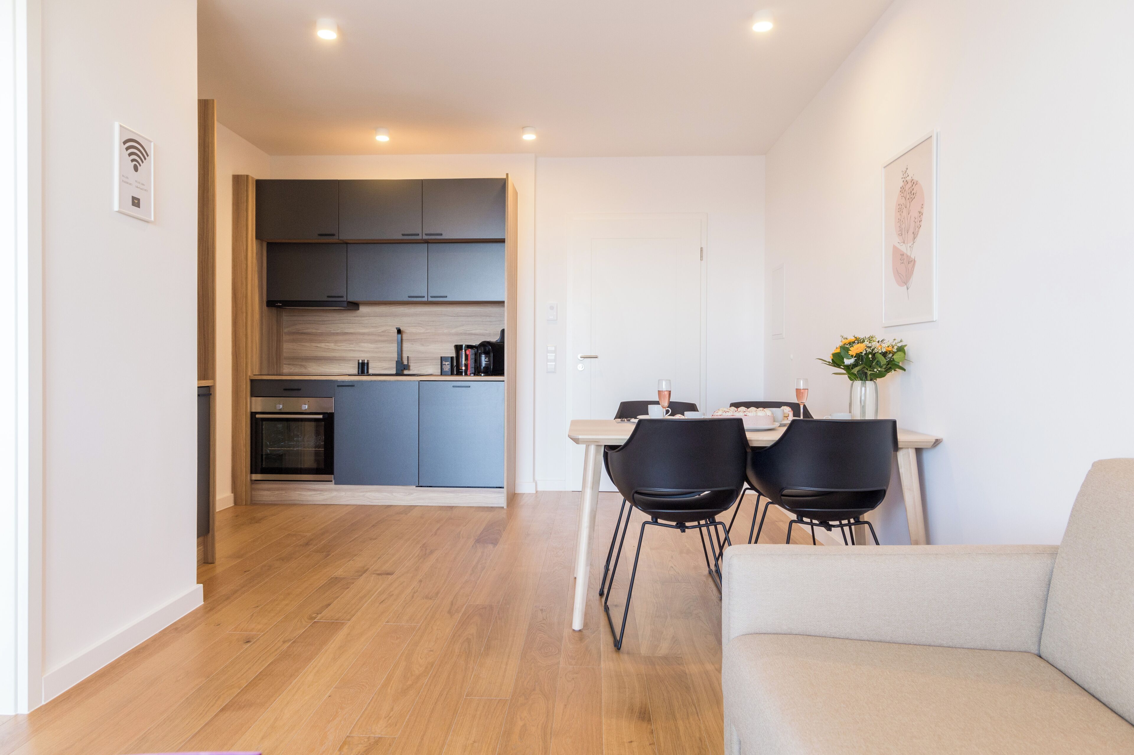 A modern kitchen with grey cabinets, a dining area with two black chairs, and a beige sofa.